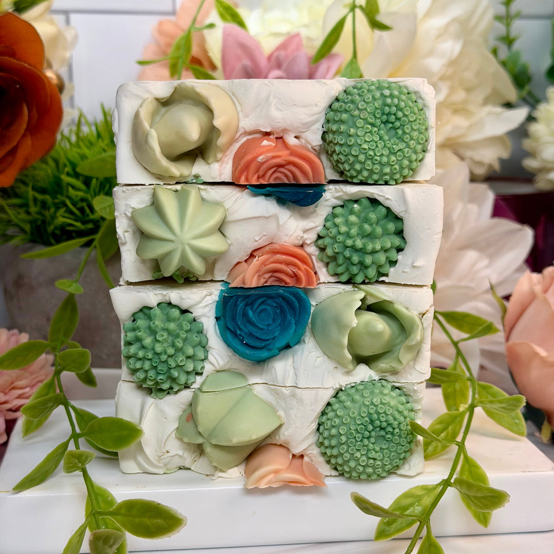 Stack of decorative soap bars with floral designs on a white surface with flowers in the background