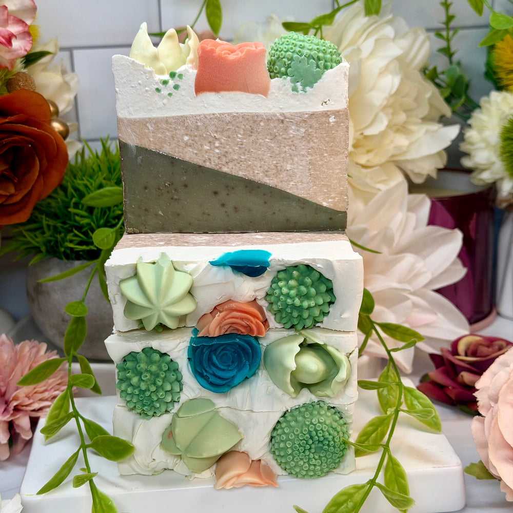 Three-tiered cake with floral and succulent decorations on a white surface with flowers and greenery.