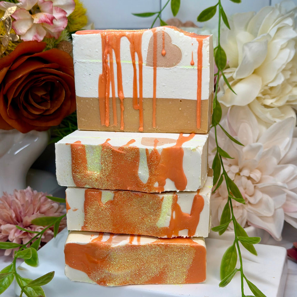 Stack of soap bars with orange and white drizzle design on a white surface with flowers and greenery.
