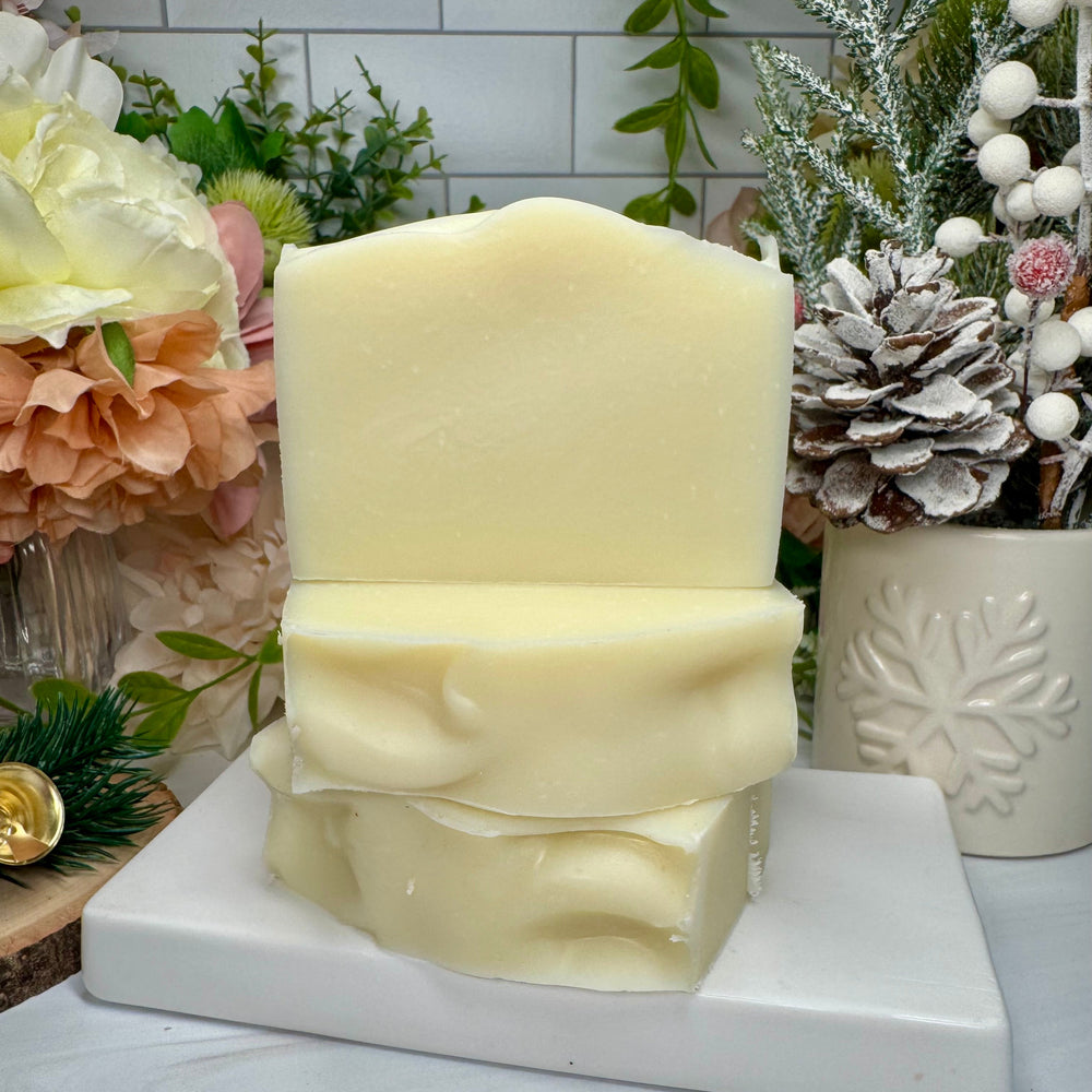 White candle on a white stand with decorative plants and flowers in the background