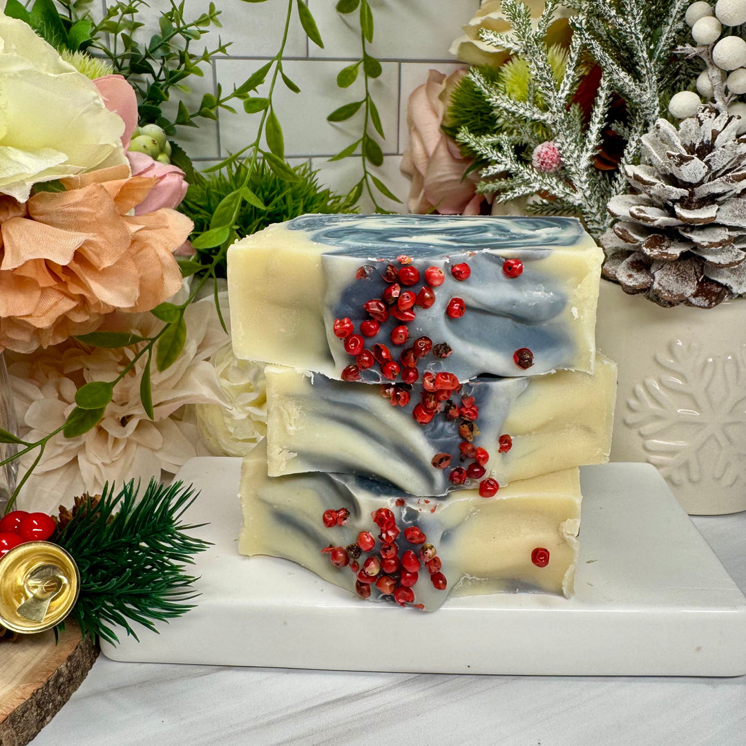 Stack of decorative soap bars with red berries on a marble surface with floral and Christmas decor.