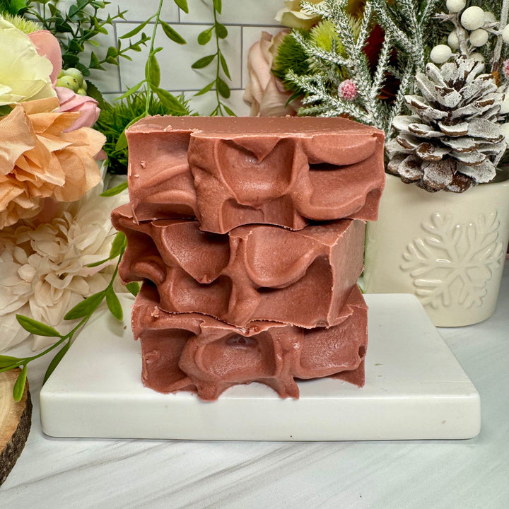 Decorative brown soap bar with intricate design on a white surface, surrounded by flowers and plants.