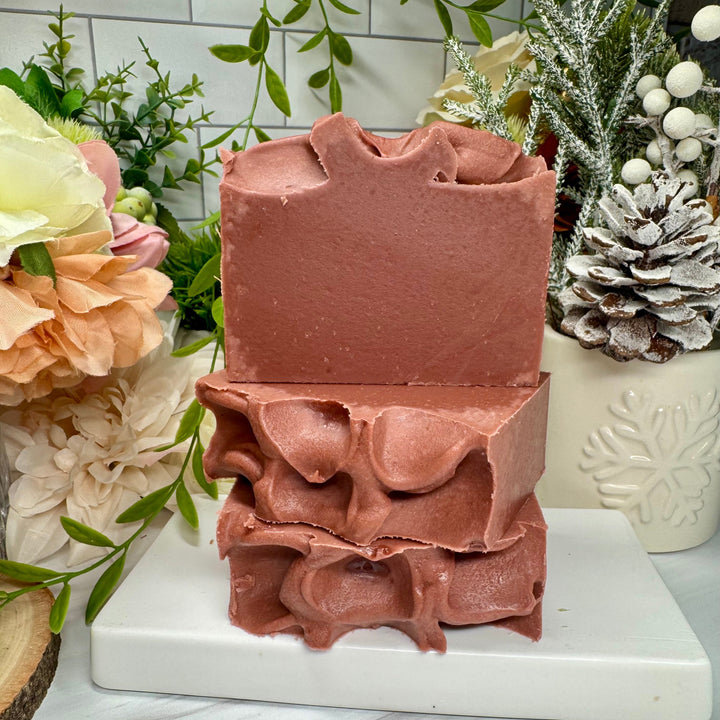 Stack of pink soap bars on a white marble stand with decorative plants in the background