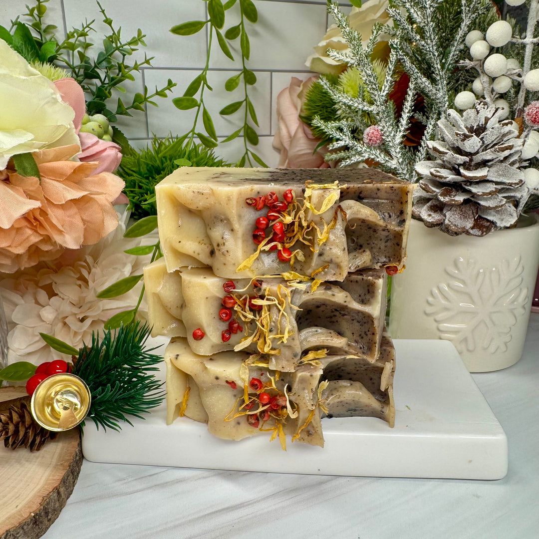 Stack of decorative soap bars with natural elements on a marble stand, surrounded by flowers and plants.