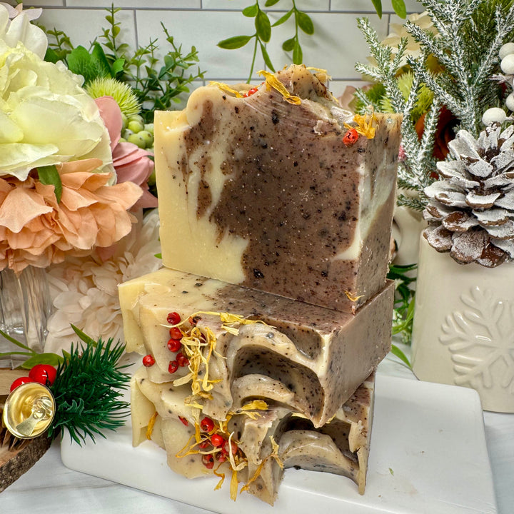 Stack of decorative soap bars with natural elements on a white marble stand, surrounded by flowers and plants.