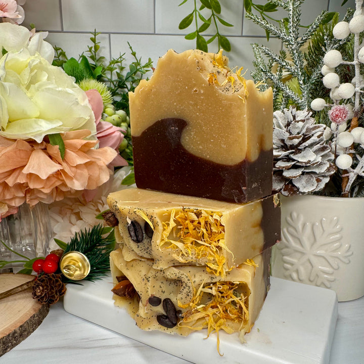 Stack of three handmade soap bars with natural ingredients on a marble slab, surrounded by decorative plants and flowers.