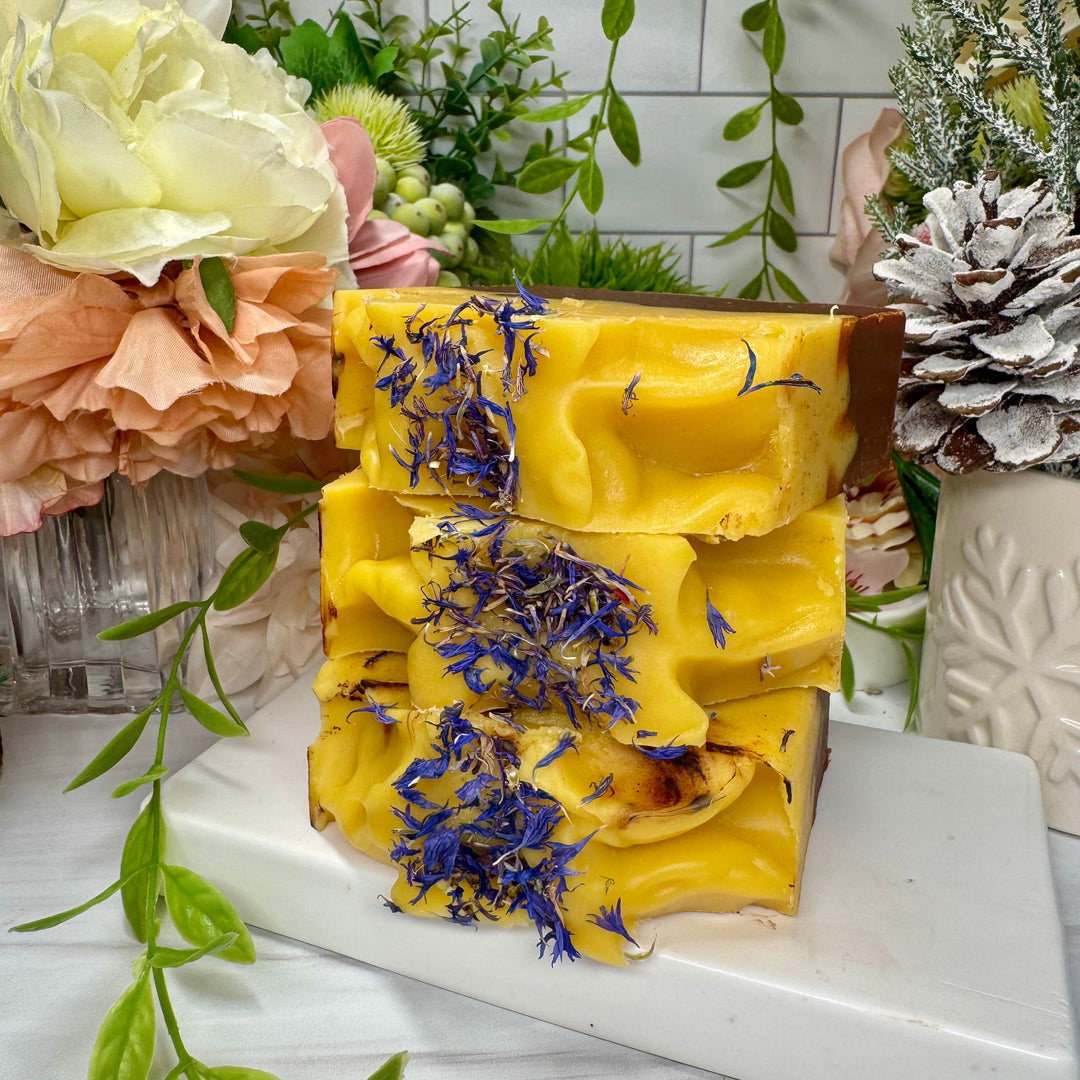 Yellow soap bar with dried flowers on a white surface with floral and greenery background