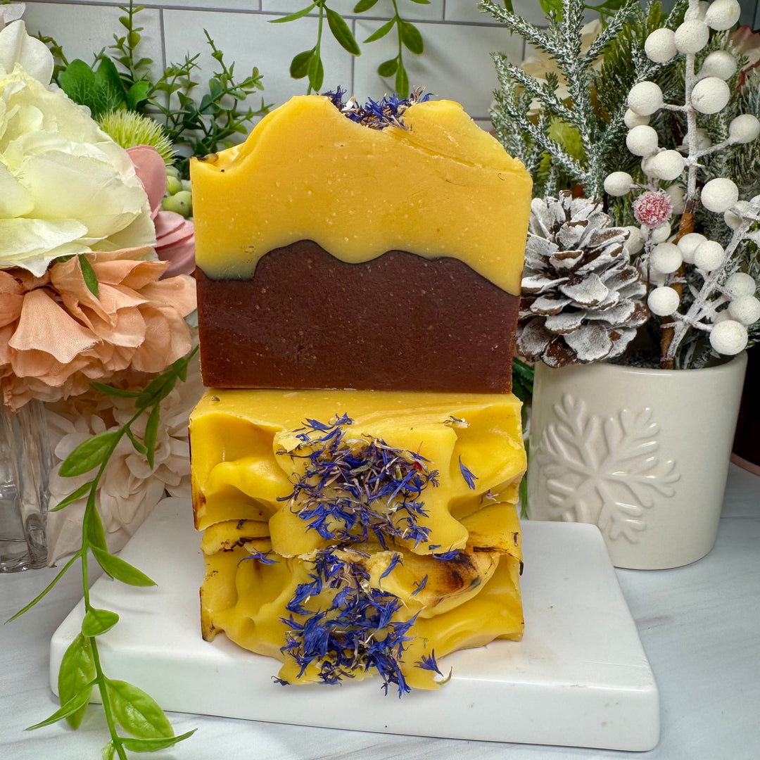 Three-layered soap with dried flowers on a white marble stand, surrounded by decorative plants.