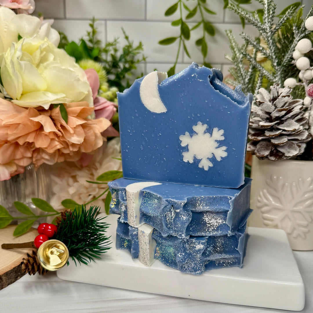 Blue decorative soap with snowflake design on a white surface with floral and greenery background