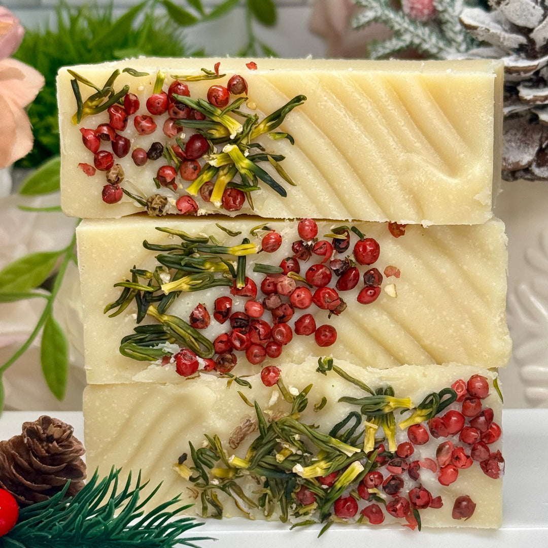Three stacked soap bars with natural elements on a white surface with greenery in the background