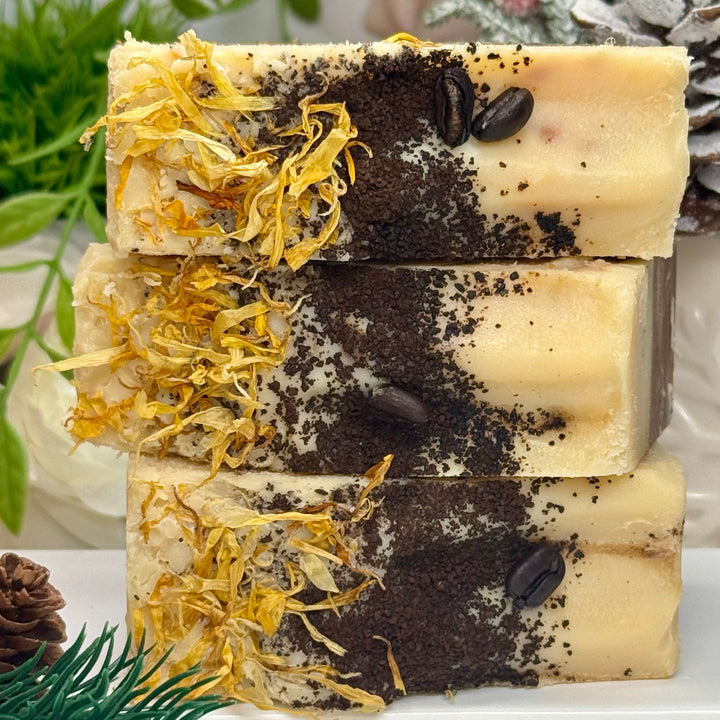 Stack of three handmade soap bars with natural ingredients on a white surface with greenery.