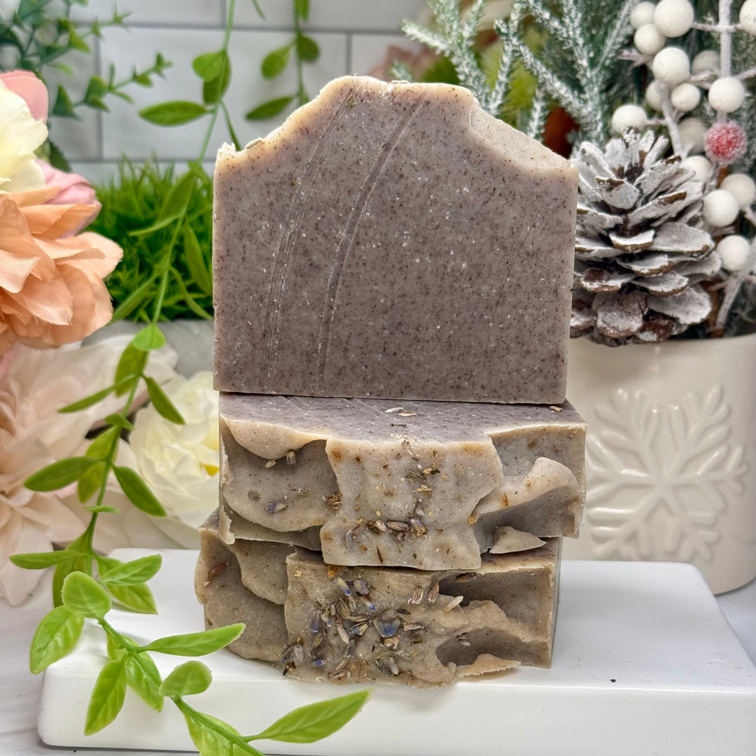 Stack of handmade soap bars on a white marble slab with decorative plants and flowers in the background.