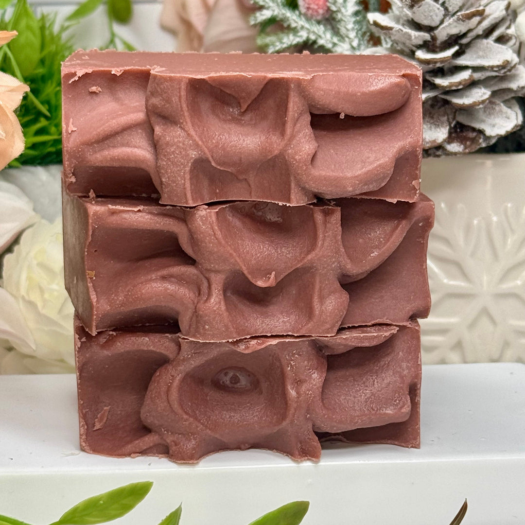 Stack of brown soap bars with decorative patterns on a white surface with greenery in the background