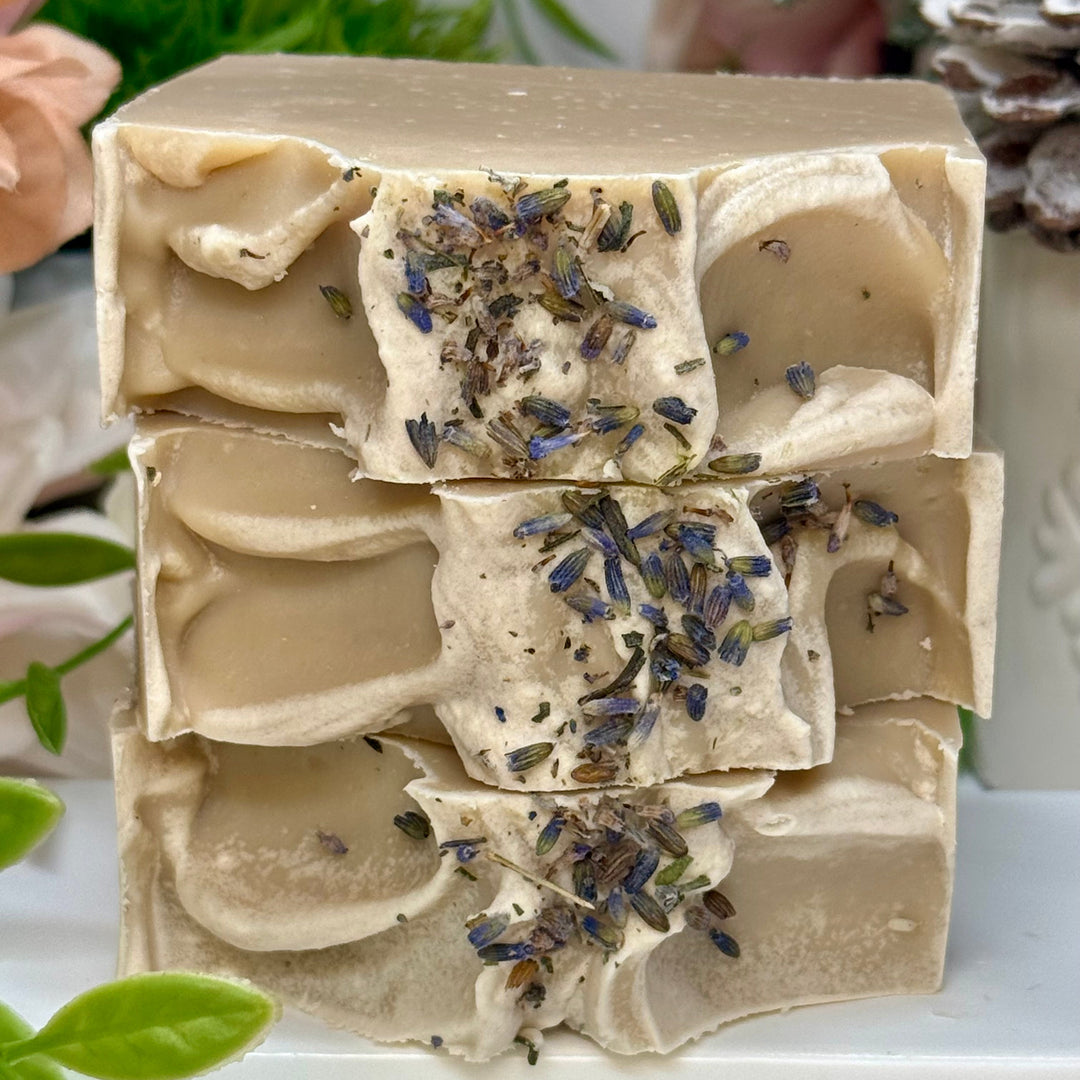 Bar of soap with lavender petals on a white surface with greenery in the background